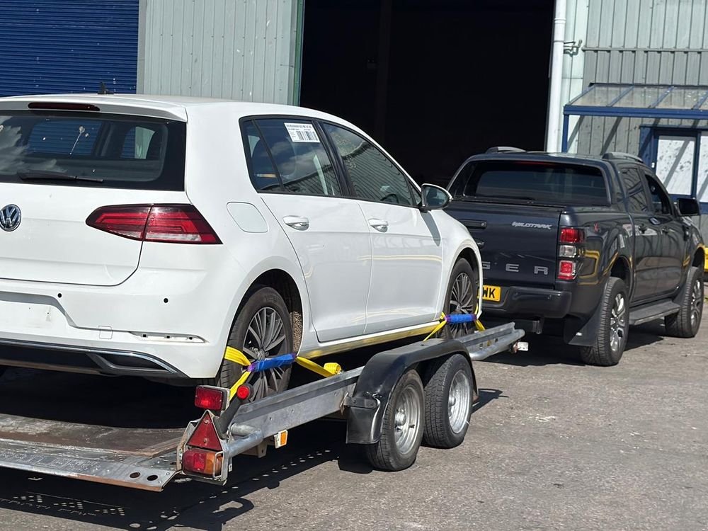 White Volkswagen Golf strapped onto a car trailer at a collection yard